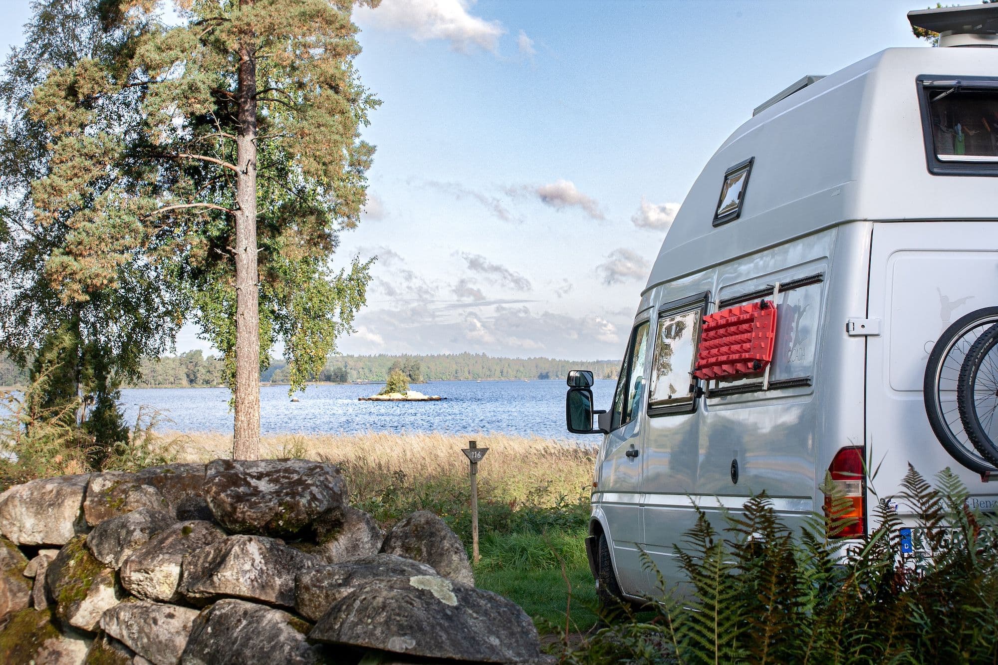 Ein weißer Mercedes Sprinter Camper steht im Wald vor einem See beim Wildcampen in Schweden